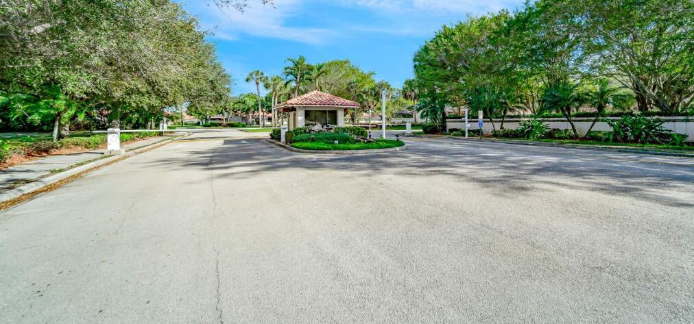 A gated community entrance features a guardhouse, palm trees, and paved roads under a blue sky — 20020 Rima Circle, Boca Raton FL 33434, BOCA RATON, FL