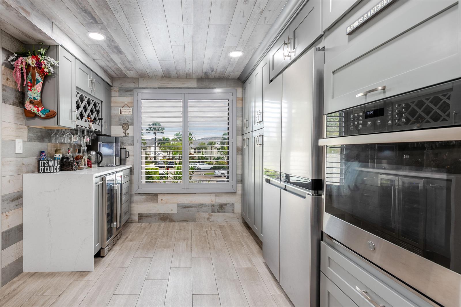 A kitchen features gray cabinetry, wood-look plank walls and ceiling, and a window with shutters — 7418 Victory Lane # 9805, Delray Beach FL 33446, DELRAY BEACH, FL