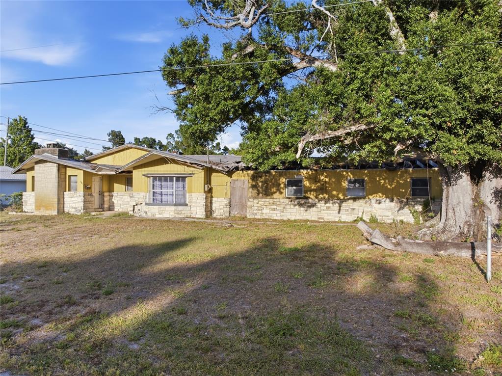A single-story house with yellow siding, stone accents, and a damaged roof under a tree — 8181 61ST LANE N, PINELLAS PARK, FL