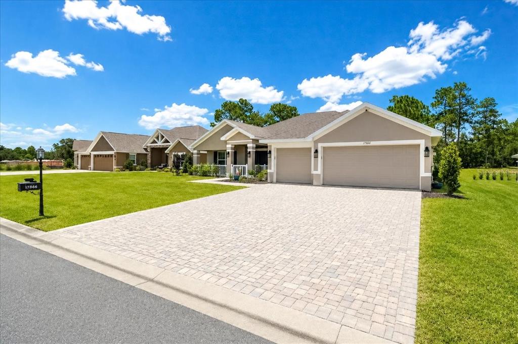A beige single-story house features a paver driveway, a three-car garage, and a grassy lawn — 17866 SW 68TH PLACE, DUNNELLON, FL
