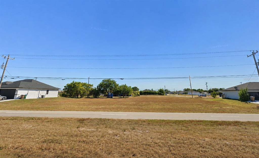 A vacant, grassy lot sits between two residential houses under a clear blue sky — 1804 KISMET PARKWAY W, CAPE CORAL, FL