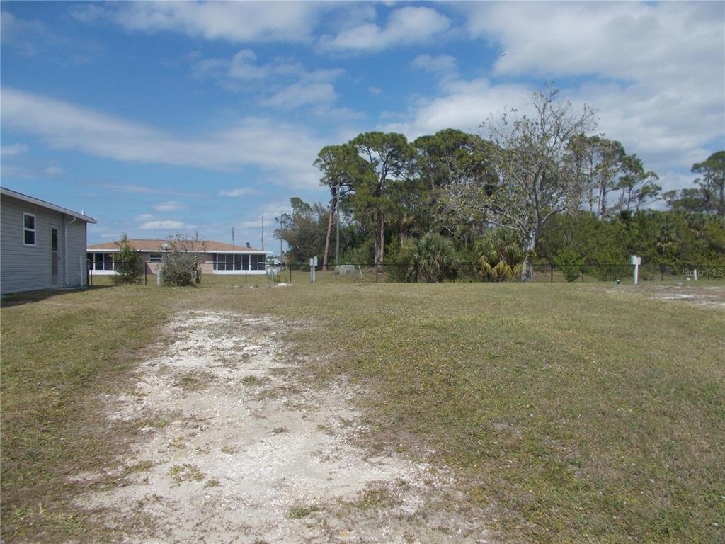 A vacant, grassy residential lot with a black chain-link fence and surrounding trees — 5552 HOLIDAY PARK BOULEVARD, NORTH PORT, FL