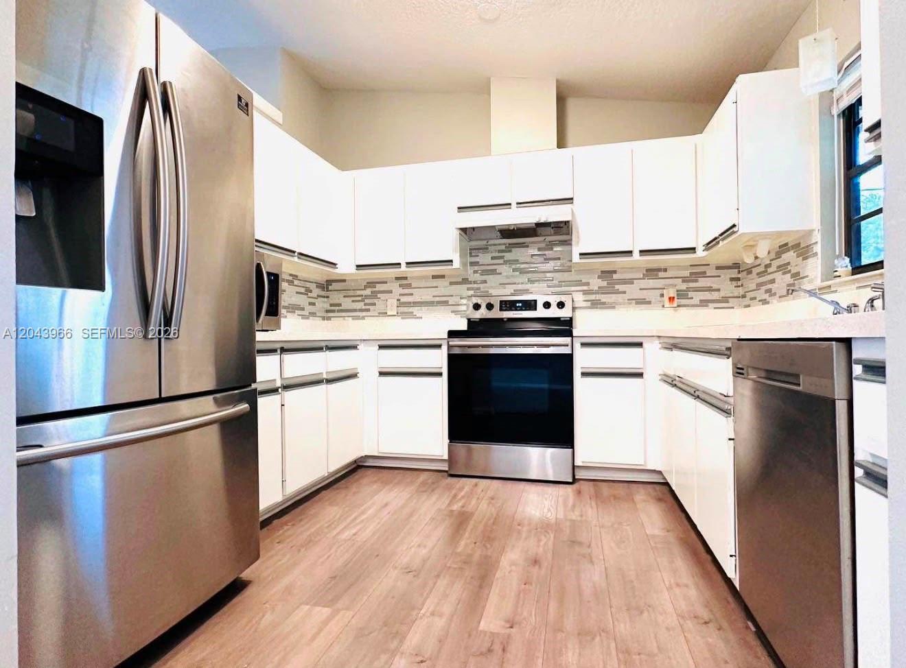 A kitchen features white cabinets, stainless steel appliances, a tiled backsplash, and wood-look flooring — 709 NW Cuxhaven St, Palm Bay FL 32907, PALM BAY, FL