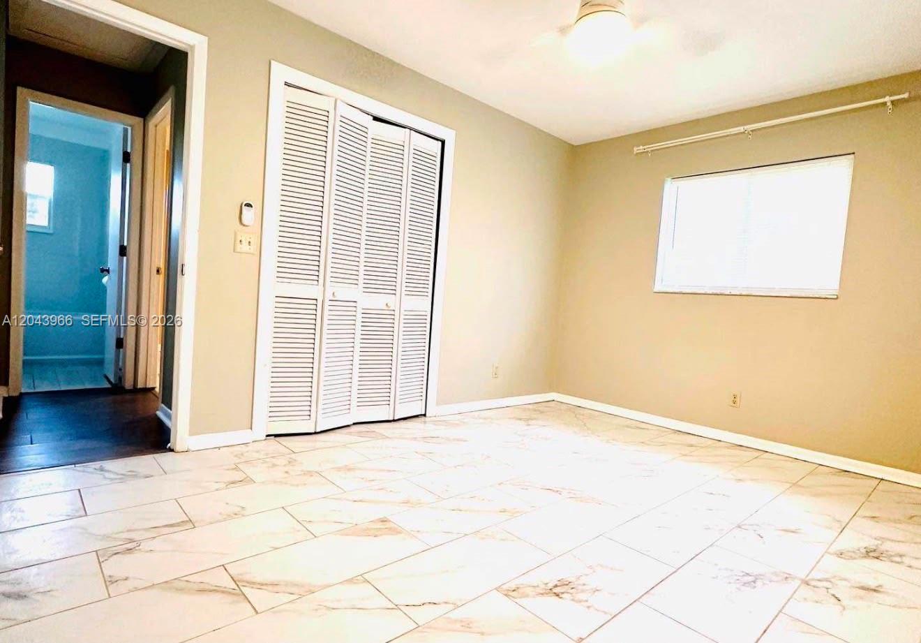 A bedroom features light-colored walls, white louvered closet doors, and white marble-patterned tile flooring — 709 NW Cuxhaven St, Palm Bay FL 32907, PALM BAY, FL