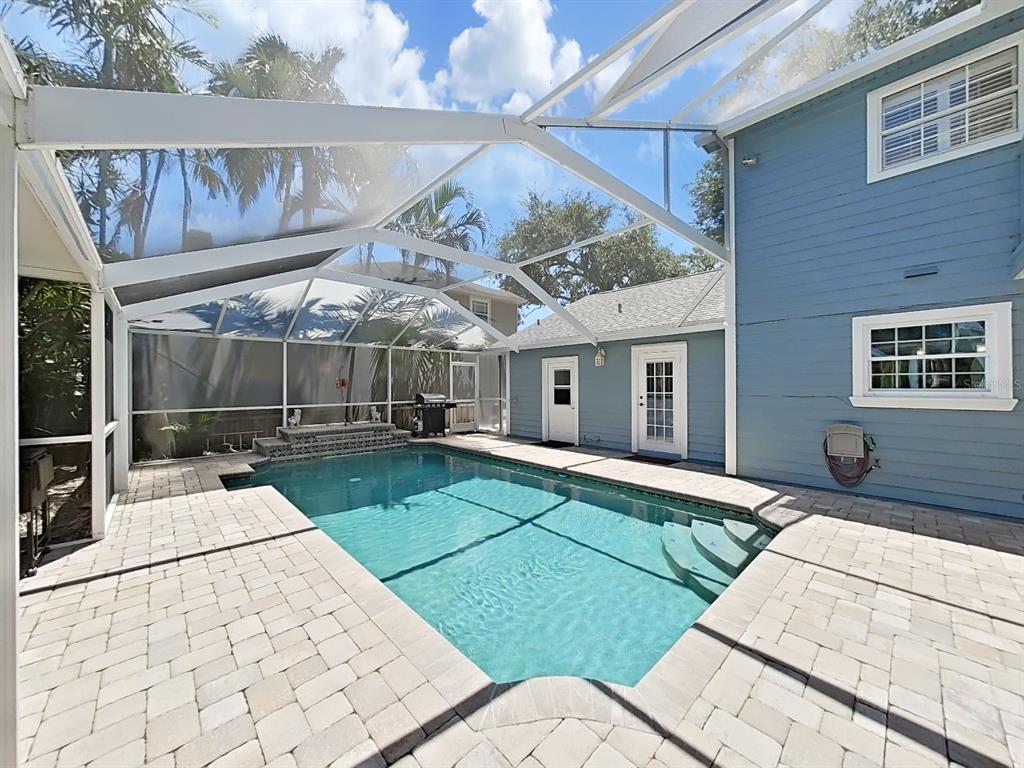 A screened-in swimming pool with a paver deck sits beside a blue two-story house — 7645 HARBOR VIEW WAY, SEMINOLE, FL