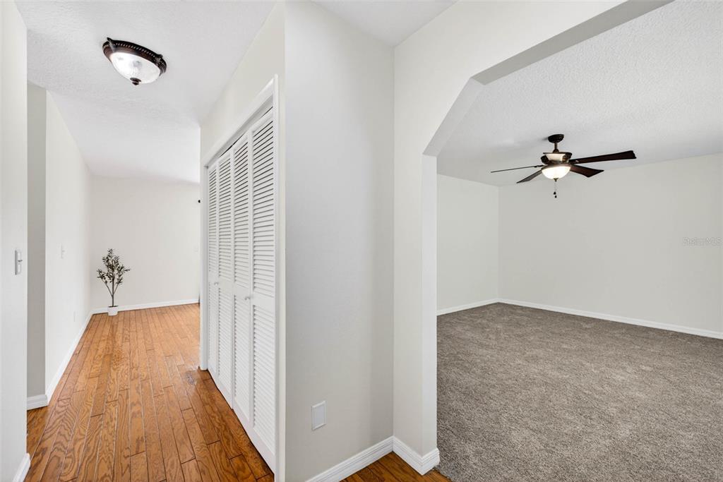 A hallway with hardwood floors and a closet leads to a carpeted room with a fan — 37121 MERIDIAN AVENUE, DADE CITY, FL