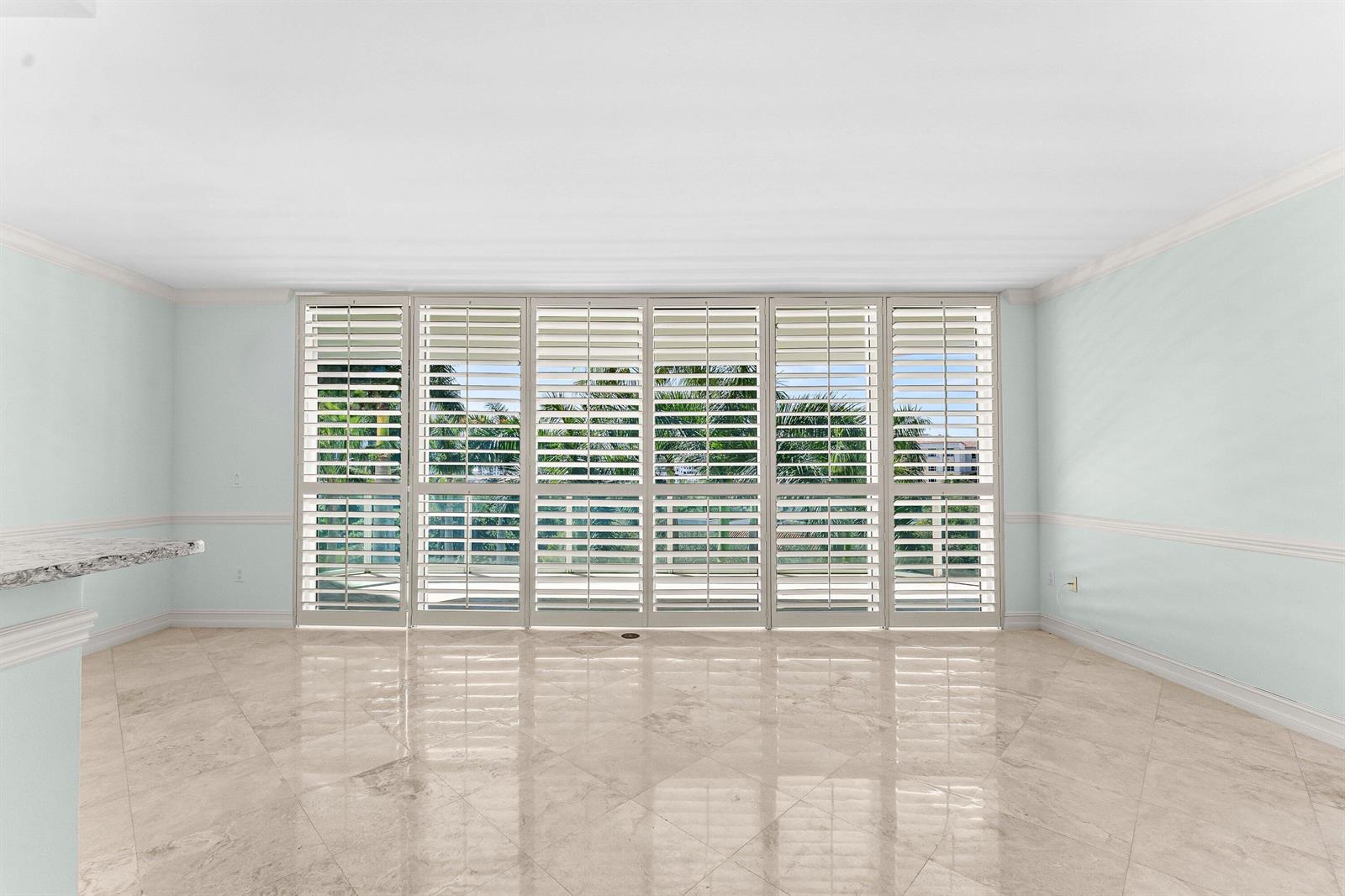 An empty room with light blue walls, marble flooring, and large white plantation shutters — 550 SE Mizner Boulevard # B501, Boca Raton FL 33432, BOCA RATON, FL
