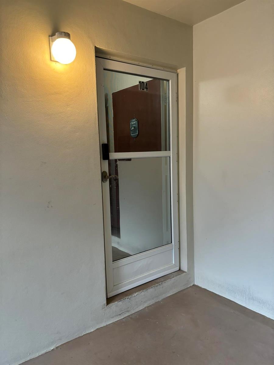 A white storm door with the number 104 is mounted on a plain exterior wall — 2302 Sunrise Boulevard # 104, Fort Pierce FL 34982, FORT PIERCE, FL