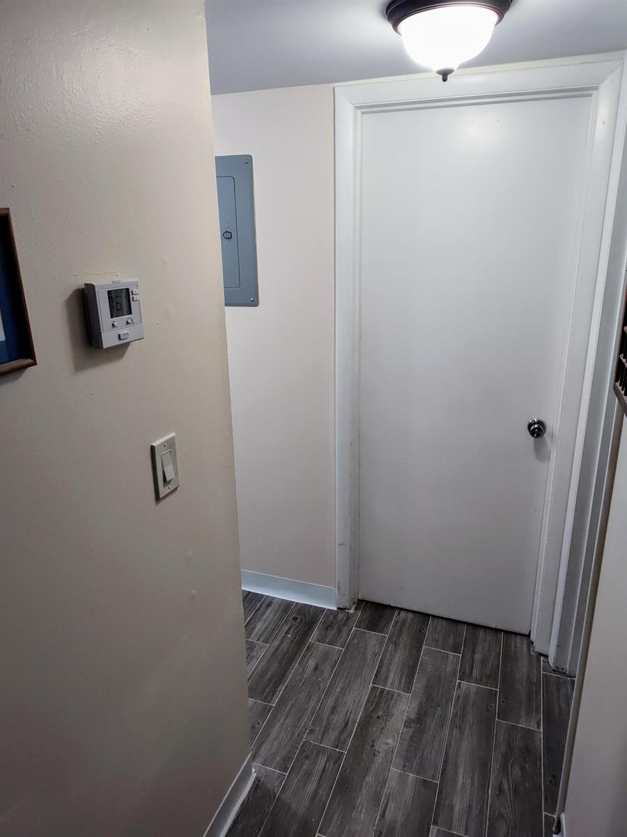 A hallway with wood-look tile flooring, a thermostat, a light switch, and a closed door — 2302 Sunrise Boulevard # 104, Fort Pierce FL 34982, FORT PIERCE, FL
