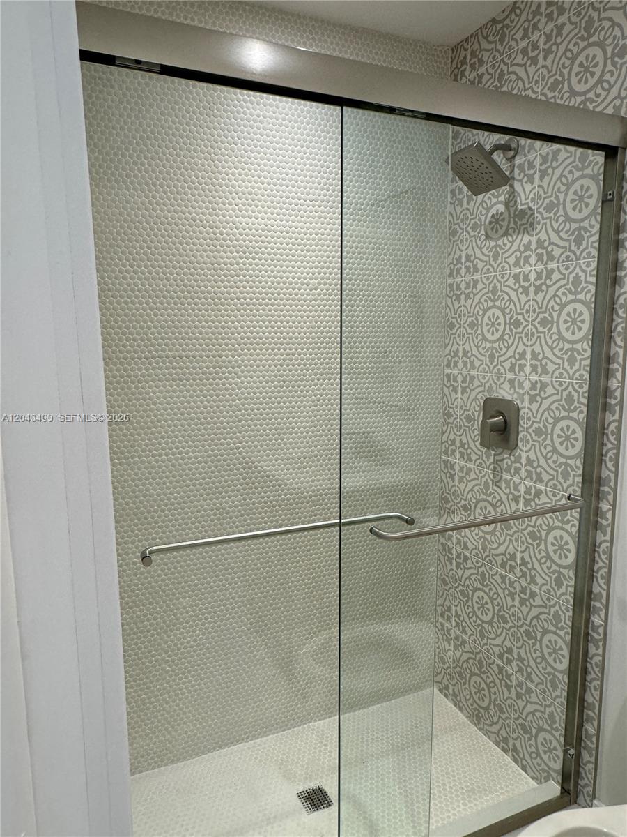 A walk-in shower features patterned wall tiles, a glass door, and a silver shower head — 951 E 32nd St, Hialeah FL 33013, HIALEAH, FL