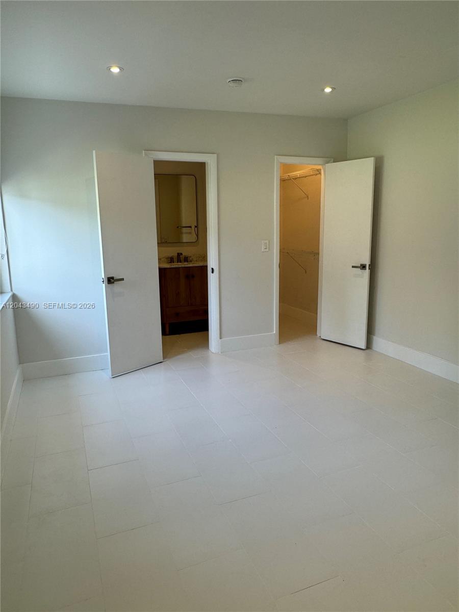 A bedroom features white tile flooring, recessed lighting, and two open doors leading to a bathroom and closet — 951 E 32nd St, Hialeah FL 33013, HIALEAH, FL