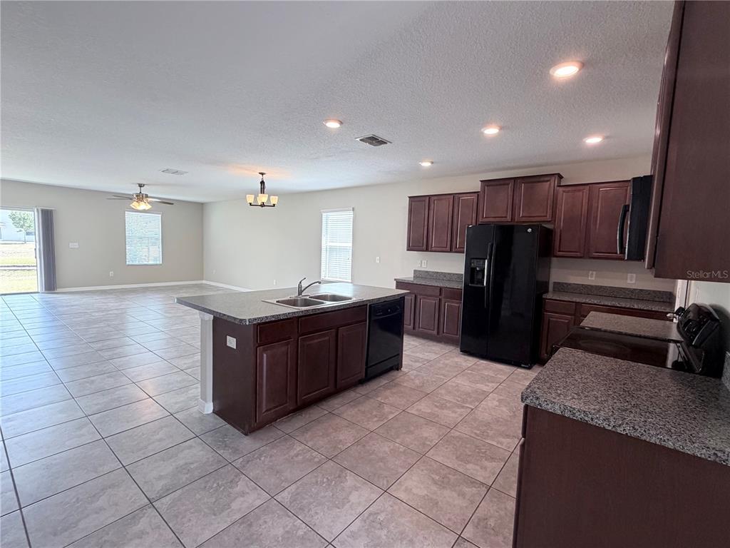 A kitchen with dark wood cabinets, granite countertops, and an island opens to a living area — 10013 CRESTED FRINGE DRIVE, RIVERVIEW, FL
