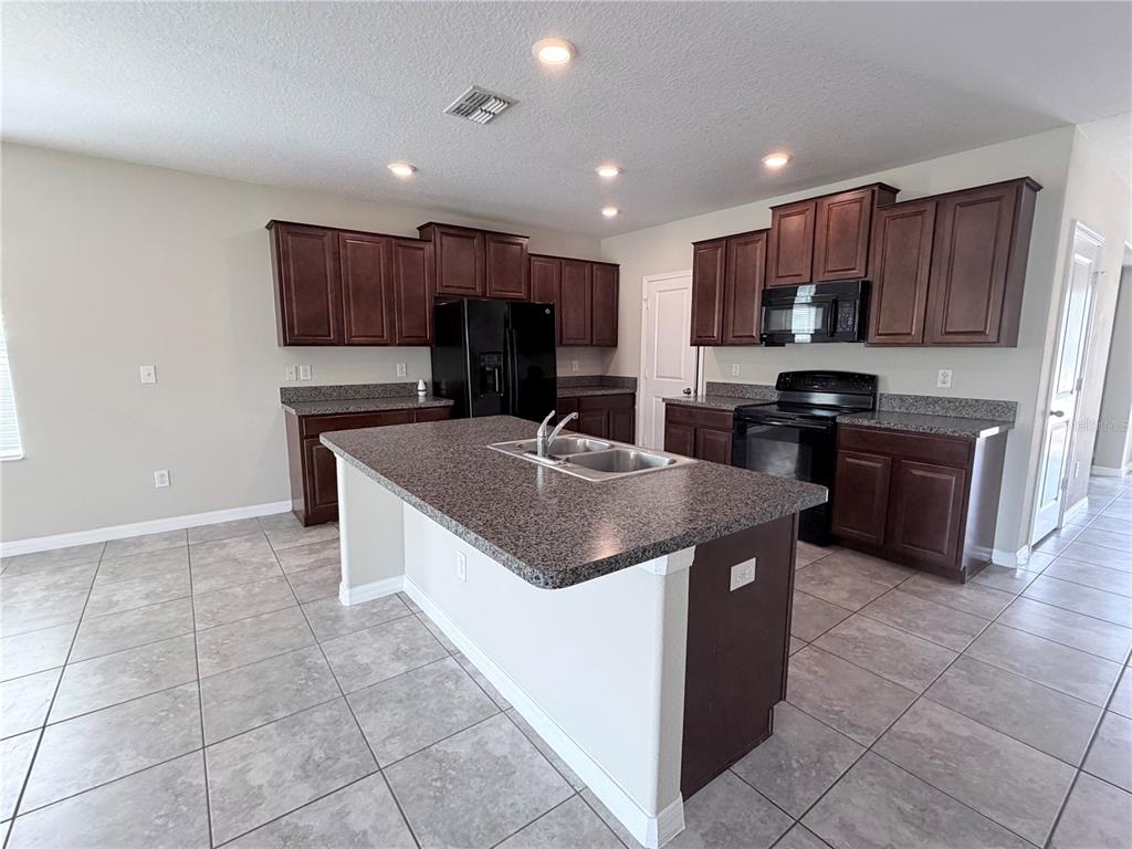 A kitchen features dark wood cabinets, granite countertops, a center island, and tile flooring — 10013 CRESTED FRINGE DRIVE, RIVERVIEW, FL