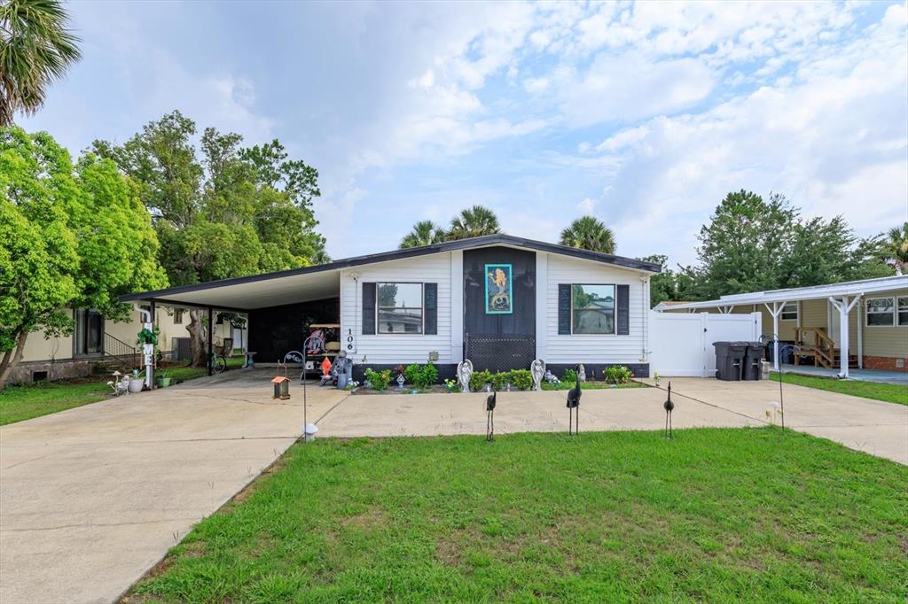 A single-story mobile home with a carport, white siding, and a dark central entryway — 106 LEISURE WORLD DRIVE N, DEBARY, FL
