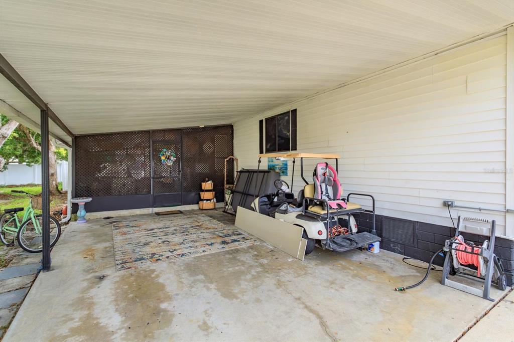 A covered concrete carport features a golf cart, a bicycle, and a screened-in entryway — 106 LEISURE WORLD DRIVE N, DEBARY, FL