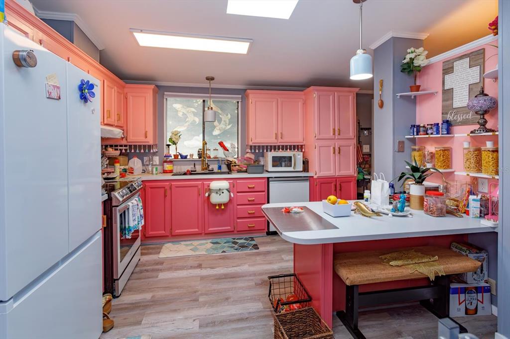 A kitchen features pink cabinets, a white island with a bench, and light wood flooring — 106 LEISURE WORLD DRIVE N, DEBARY, FL