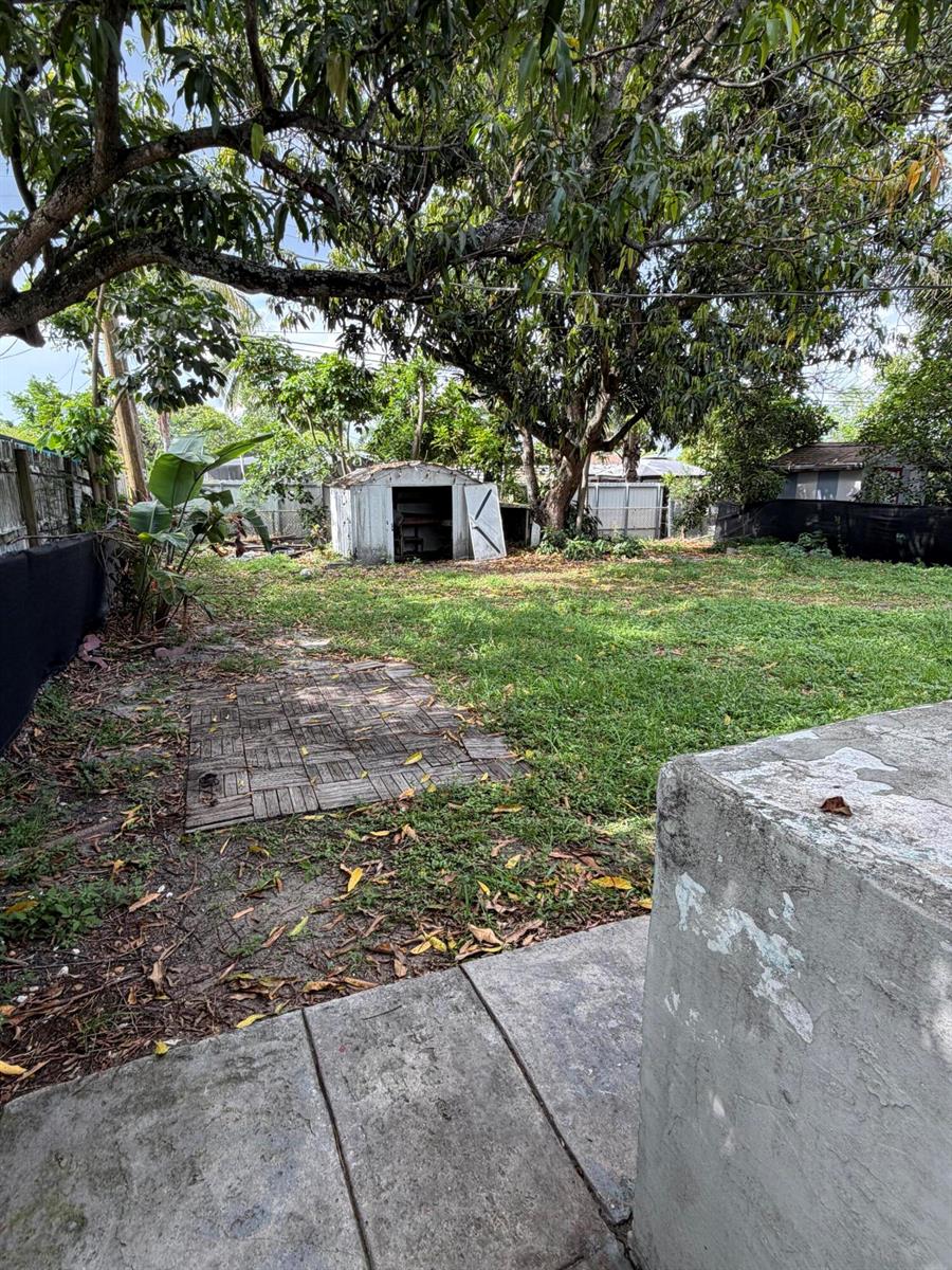 A backyard features a grassy lawn, a small metal shed, and a paved patio area — 6129 SW 22nd Street, Miramar FL 33023, MIRAMAR, FL