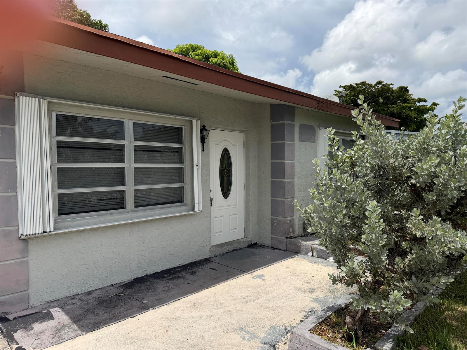The exterior of a single-story house features a white front door and a large window — 6129 SW 22nd Street, Miramar FL 33023, MIRAMAR, FL