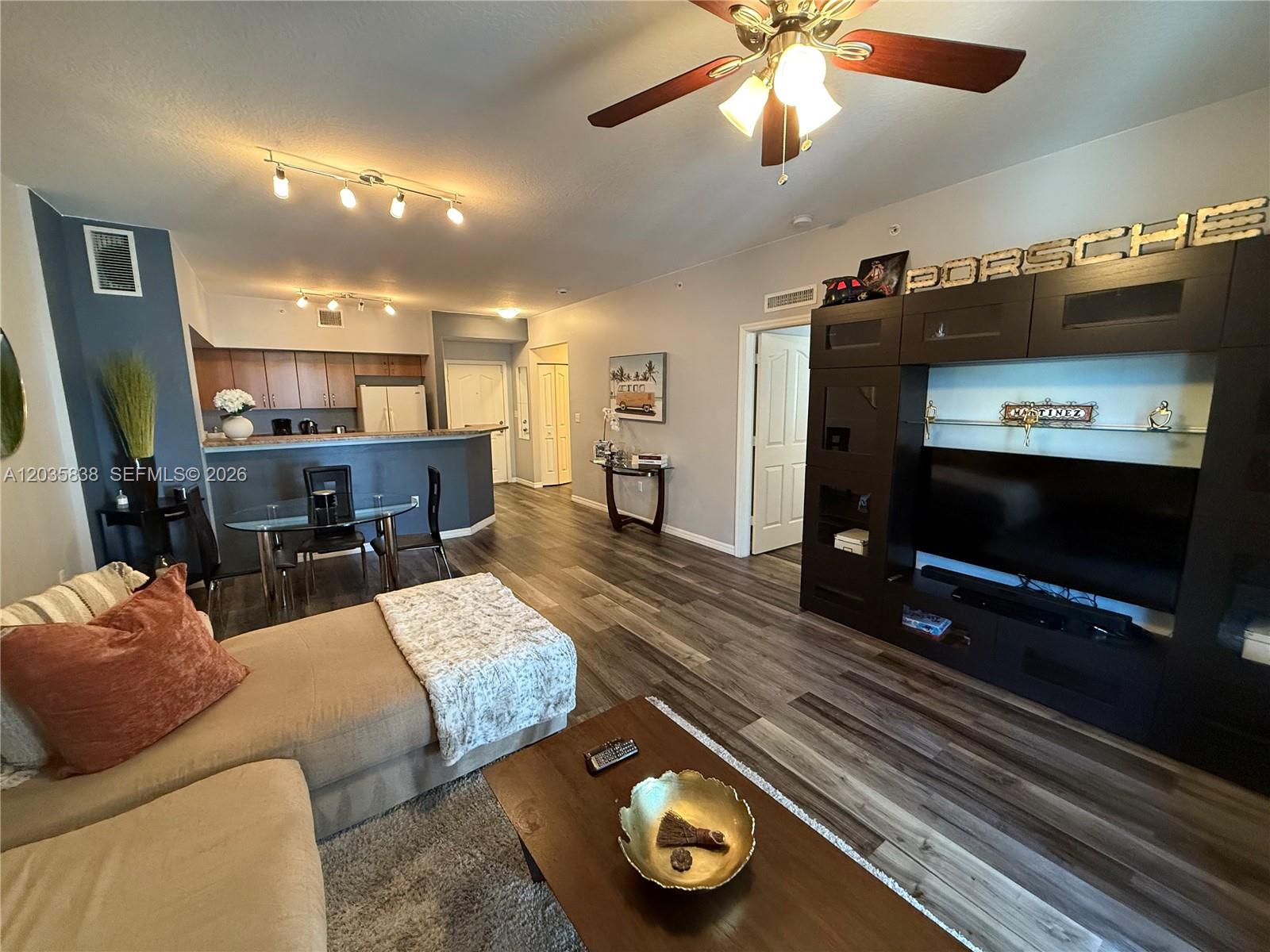 A living room with wood-look flooring, a dark entertainment center, and an open kitchen — 250 NE 3rd Ave # 1210, Delray Beach FL 33444, DELRAY BEACH, FL