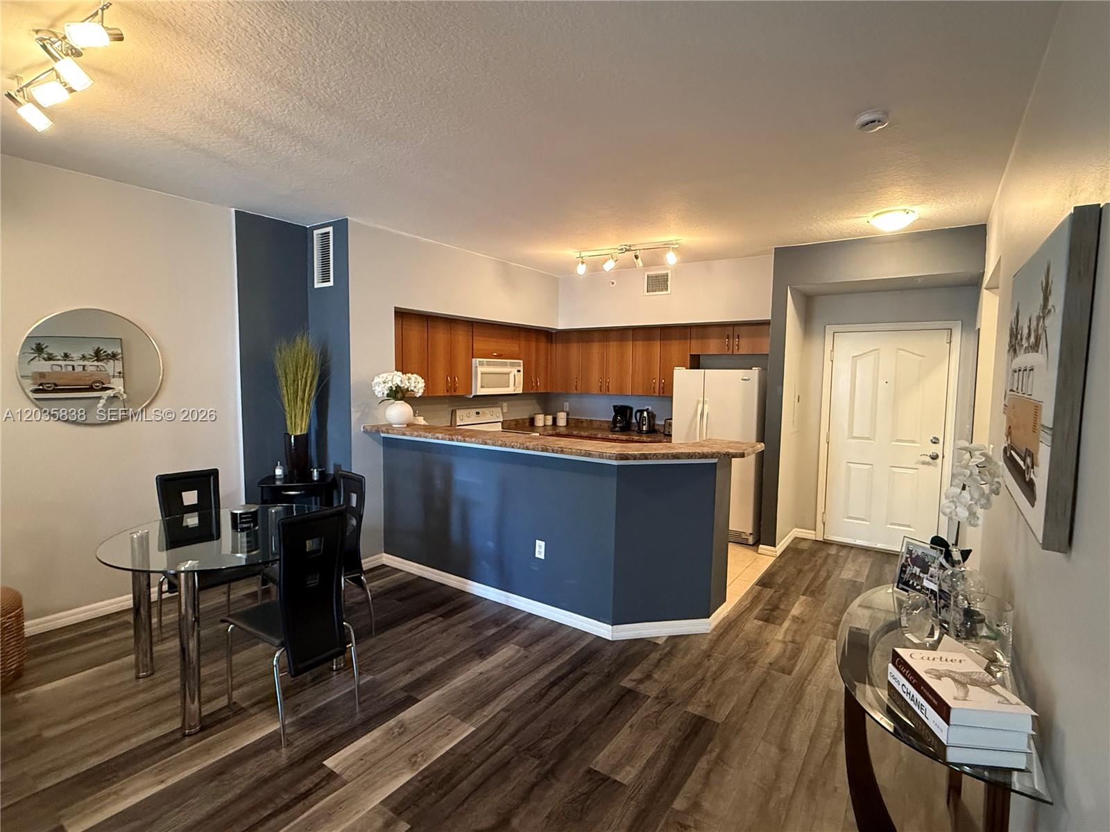 A kitchen with wood cabinets and a dark blue island opens to a dining area — 250 NE 3rd Ave # 1210, Delray Beach FL 33444, DELRAY BEACH, FL
