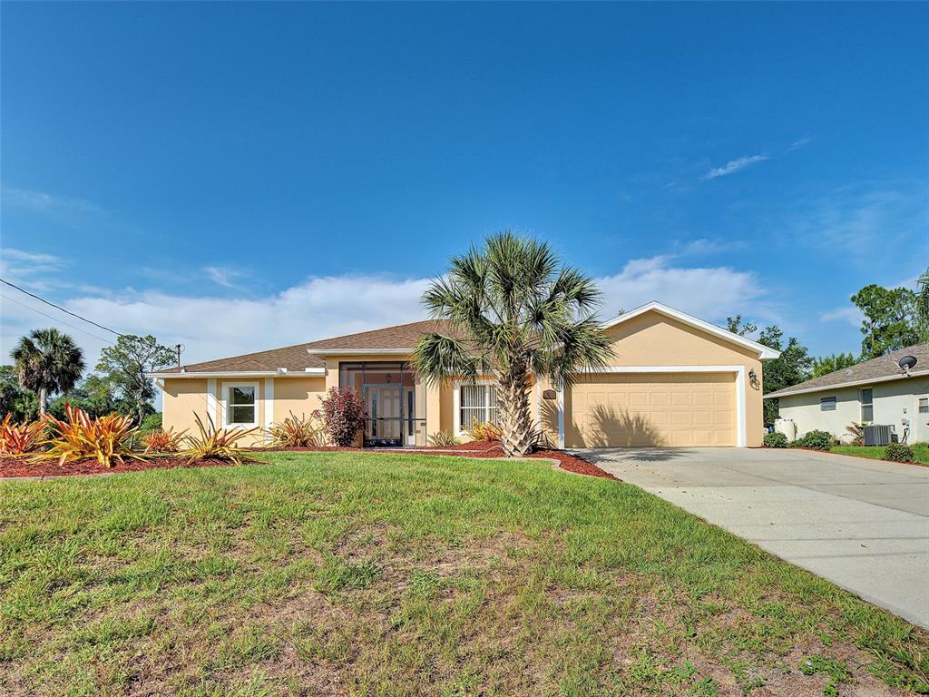 A single-story suburban house with a tan exterior, two-car garage, and a front palm tree — 1115 URMEY LANE, NORTH PORT, FL
