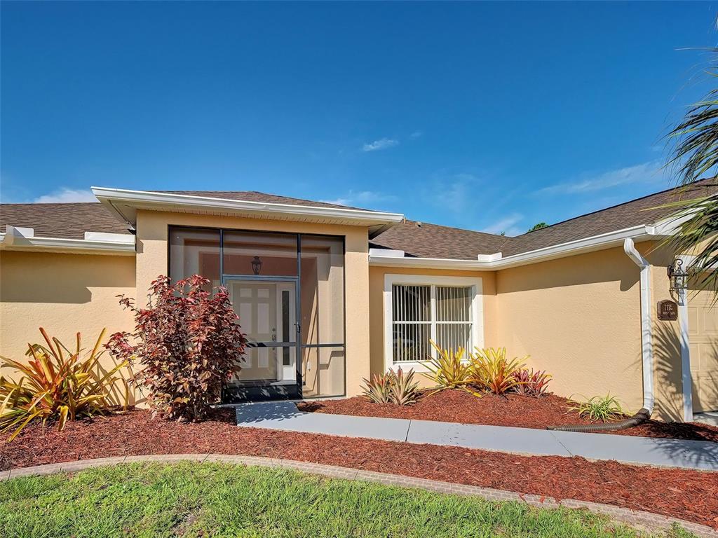 The exterior of a tan house features a screened front entryway and a landscaped garden bed — 1115 URMEY LANE, NORTH PORT, FL