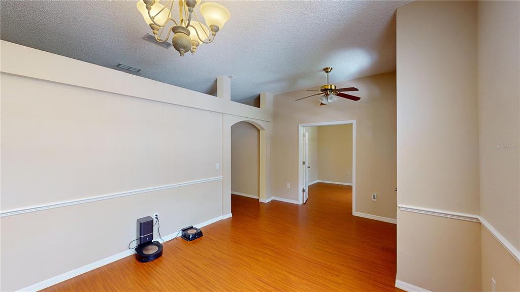A room with wood-look flooring, beige walls, a ceiling fan, and a chandelier — 26 LLOLEETA PATH, PALM COAST, FL