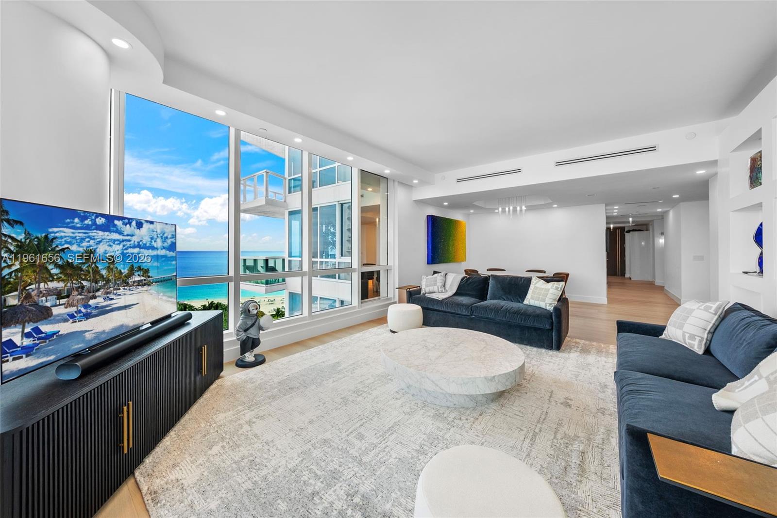 A modern living room features blue sofas, a marble coffee table, and floor-to-ceiling ocean views — 100 S Pointe Dr, Miami Beach FL 33139, MIAMI BEACH, FL
