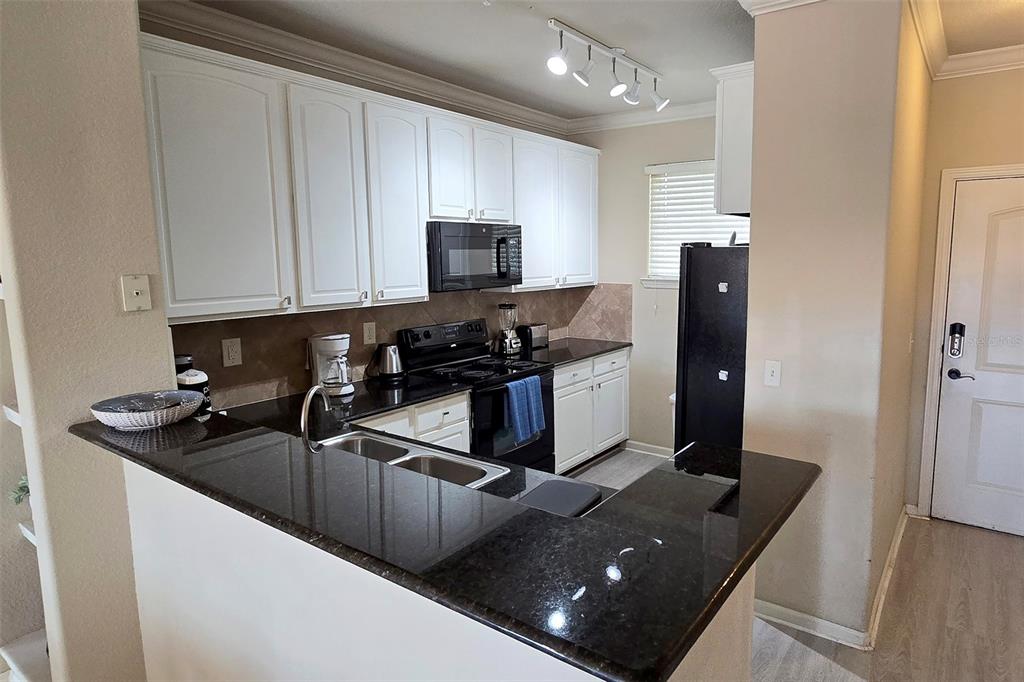 A kitchen features white cabinets, black countertops, a black appliance suite, and a breakfast bar — 912 CHARO PARKWAY UNIT 233, DAVENPORT, FL