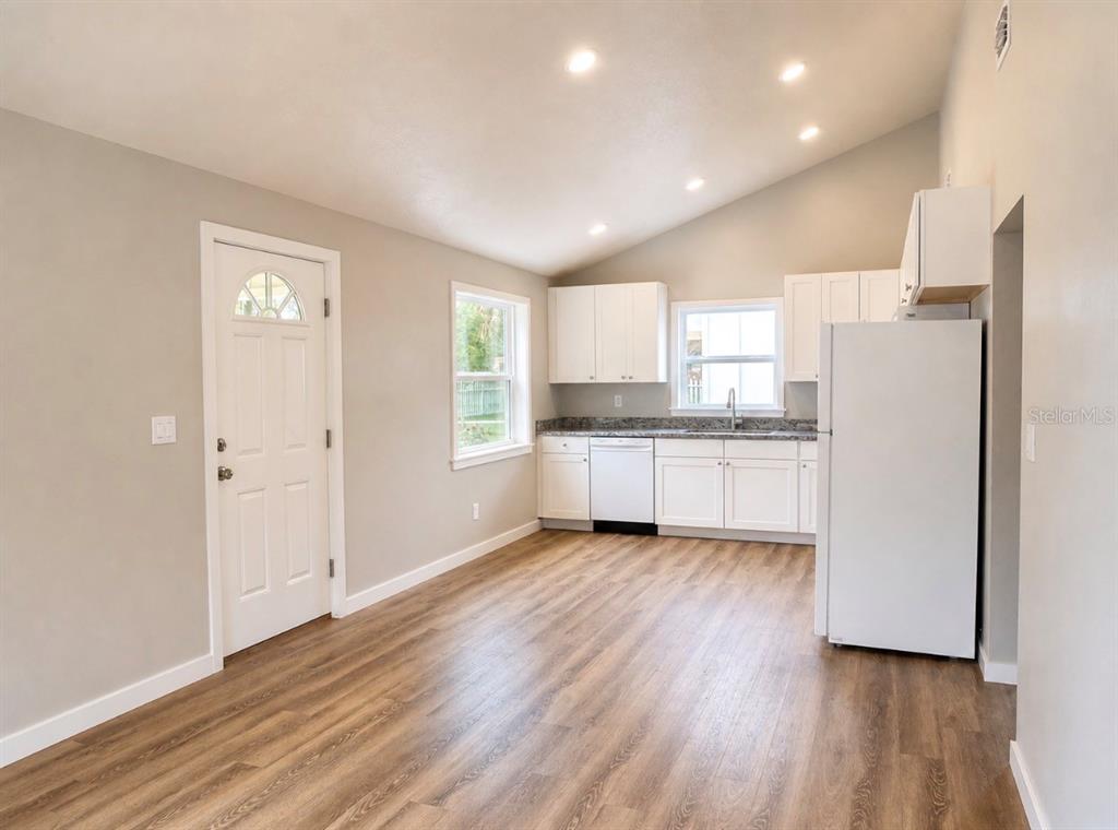 A kitchen with white cabinets, stainless steel appliances, and wood-look flooring under a vaulted ceiling — 351 N MAIN AVENUE, GROVELAND, FL