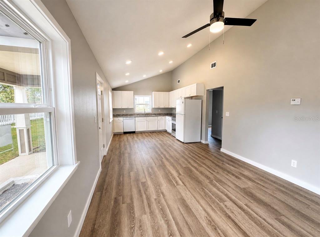 A kitchen with white cabinets, stainless steel appliances, and wood-look flooring under a vaulted ceiling — 351 N MAIN AVENUE, GROVELAND, FL
