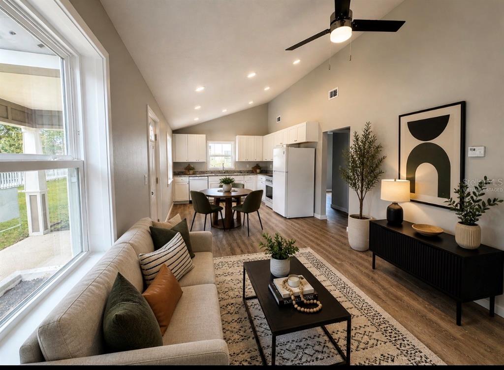 An open-concept living and dining area features a vaulted ceiling, white cabinetry, and wood flooring — 351 N MAIN AVENUE, GROVELAND, FL