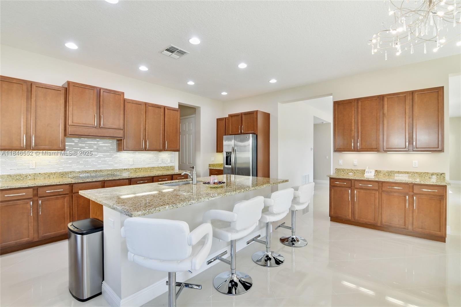 A kitchen features wood cabinets, granite countertops, a central island with bar stools, and tile floors — 12137 Boca Reserve Ln, Boca Raton FL 33428, BOCA RATON, FL