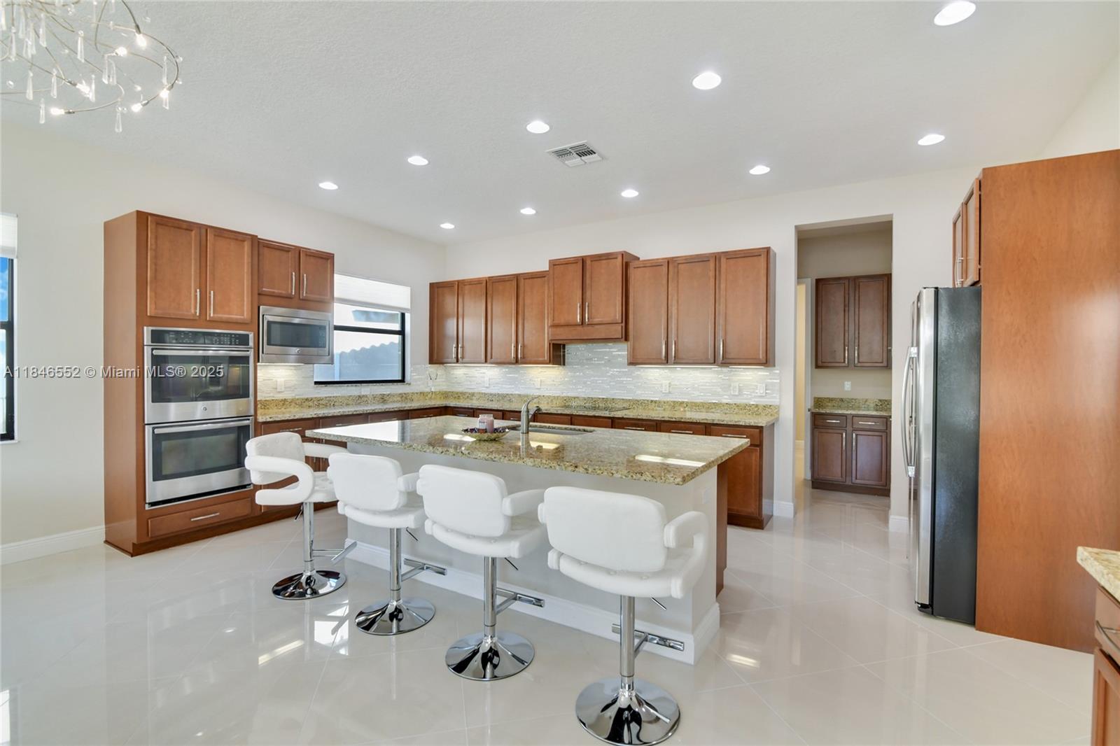 A kitchen features wood cabinets, granite countertops, a central island, and four white bar stools — 12137 Boca Reserve Ln, Boca Raton FL 33428, BOCA RATON, FL