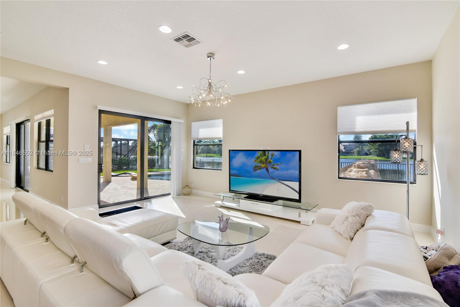 A bright living room features white leather sofas, a glass coffee table, and sliding glass doors — 12137 Boca Reserve Ln, Boca Raton FL 33428, BOCA RATON, FL