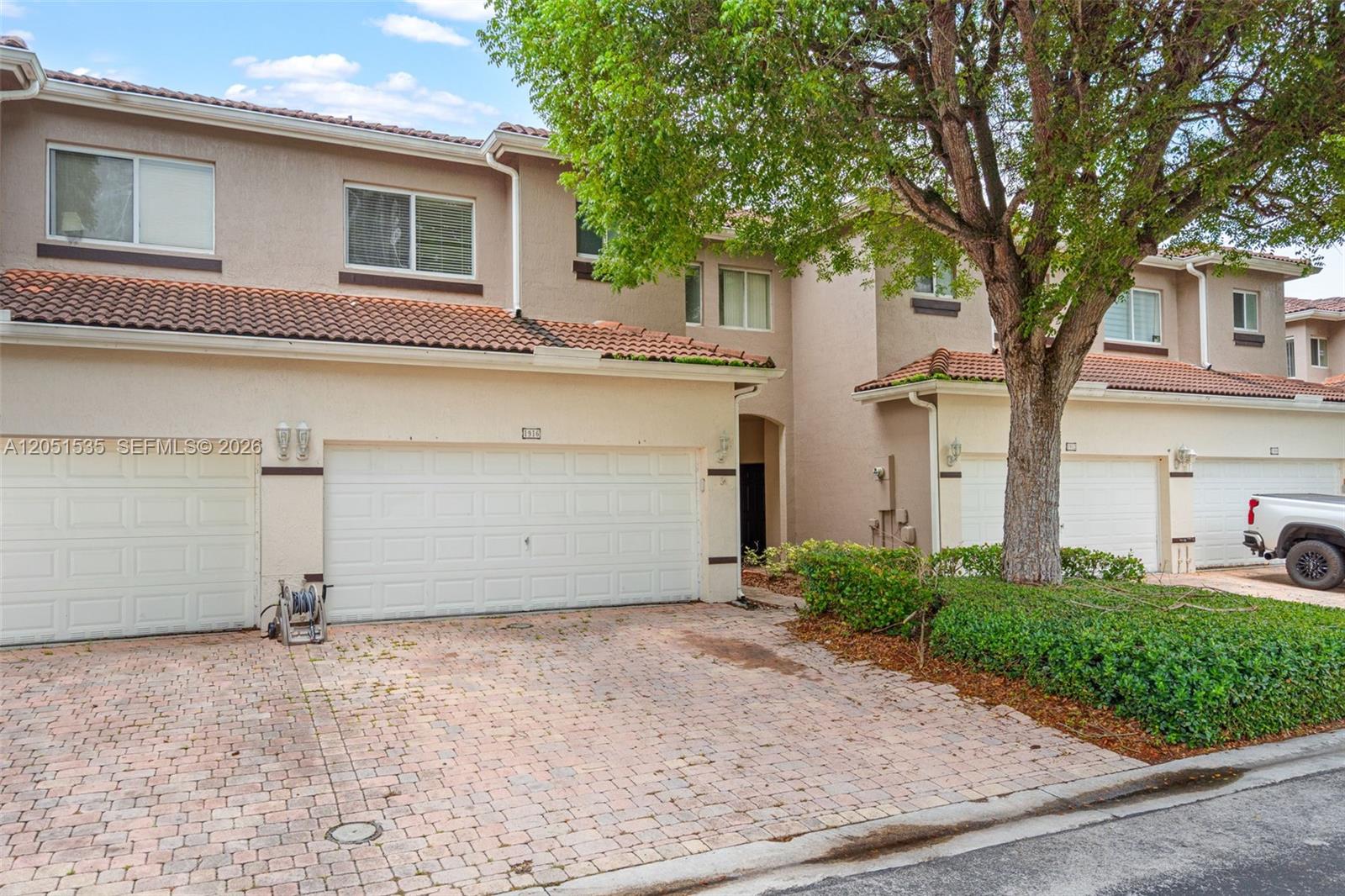 A two-story townhouse features a beige stucco exterior, a tiled roof, and a brick driveway — 1916 SE 23rd Ave, Homestead FL 33035, HOMESTEAD, FL