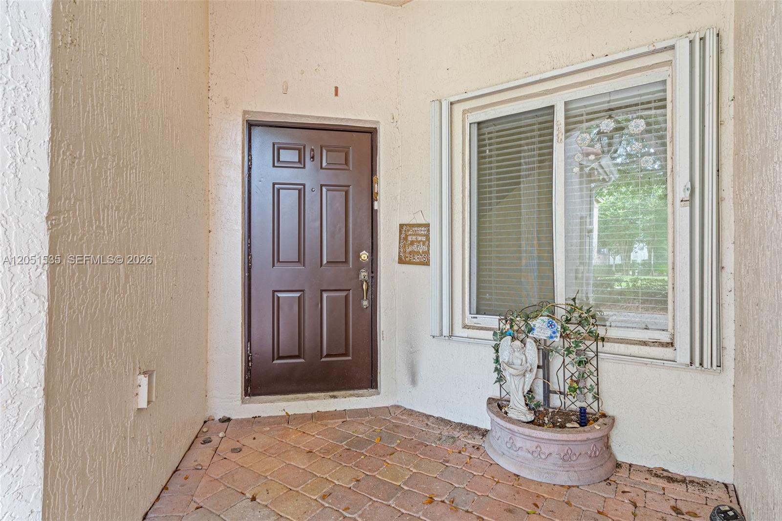 A brown front door and a window with blinds are on a brick-paved porch — 1916 SE 23rd Ave, Homestead FL 33035, HOMESTEAD, FL