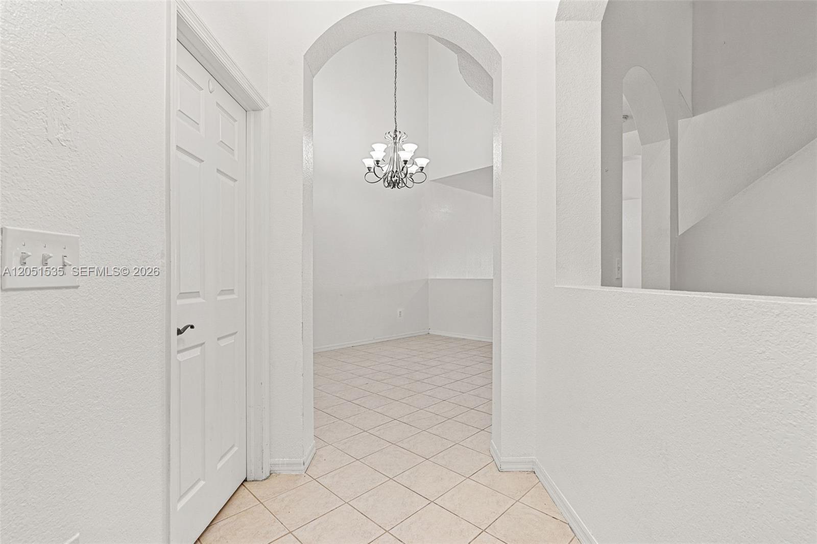 A white hallway with tiled floors leads through an arched opening to a dining area — 1916 SE 23rd Ave, Homestead FL 33035, HOMESTEAD, FL