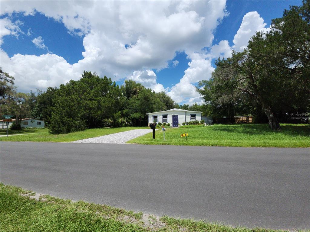 A single-story house with a gravel driveway sits on a grassy lot under a cloudy sky — 8569 W ADMIRAL BYRD LANE, CRYSTAL RIVER, FL