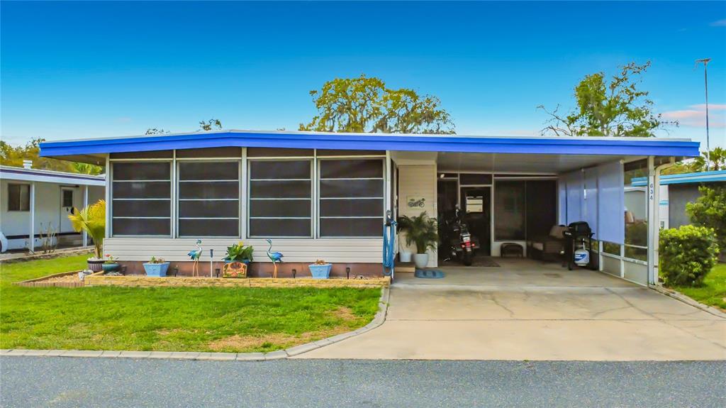 A single-story mobile home with a blue roof, screened-in porch, and an attached carport — 634 MISTI DRIVE, LEESBURG, FL