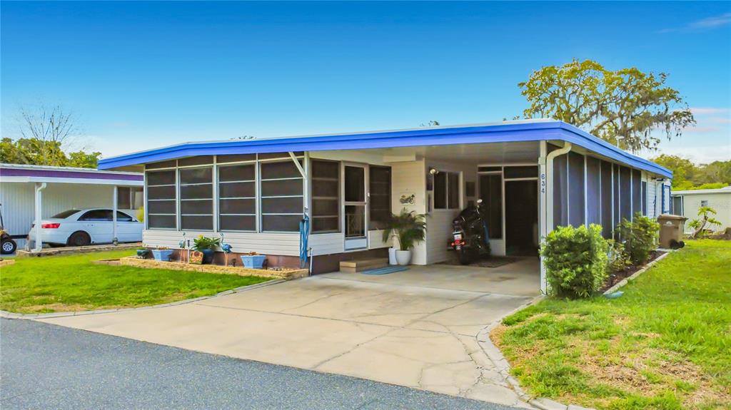 A single-story manufactured home with a screened-in porch, carport, and a motorcycle parked inside — 634 MISTI DRIVE, LEESBURG, FL