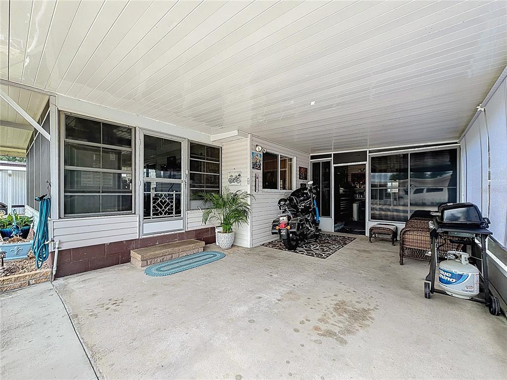 A covered concrete patio features a motorcycle, outdoor furniture, and a propane grill — 634 MISTI DRIVE, LEESBURG, FL