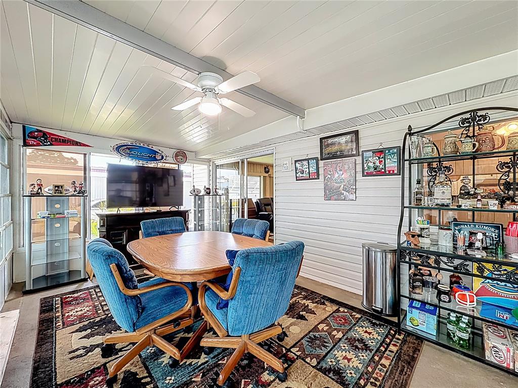A sunroom features a round wooden table, blue chairs, a rug, and a metal shelving unit — 634 MISTI DRIVE, LEESBURG, FL