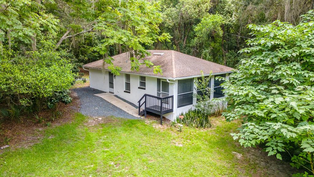 A white, single-story house with a brown roof sits in a wooded, grassy yard — 497 W BERESFORD ROAD, DELAND, FL