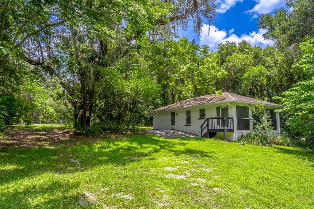 A single-story house with a small deck sits in a grassy, tree-filled yard — 497 W BERESFORD ROAD, DELAND, FL