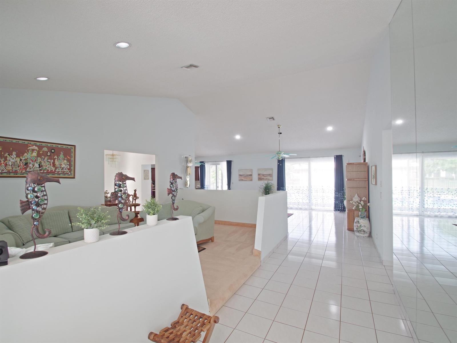 A living room with a sunken carpeted seating area, white tile floors, and vaulted ceilings — 6300 NW 60th Way, Parkland FL 33067, PARKLAND, FL
