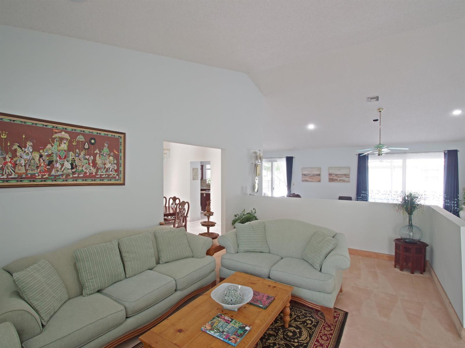A living room features two light green sofas, a wooden coffee table, and vaulted ceilings — 6300 NW 60th Way, Parkland FL 33067, PARKLAND, FL