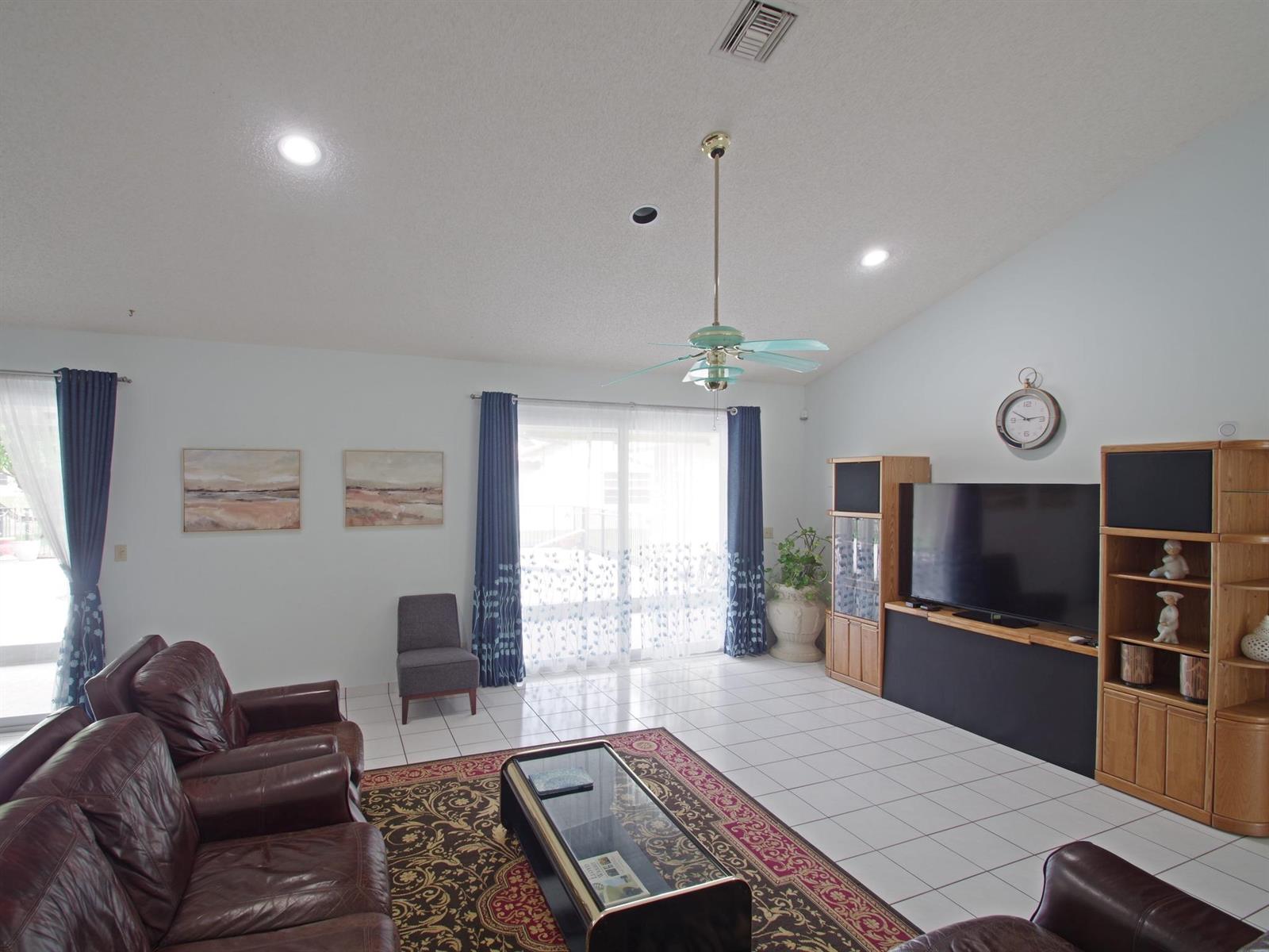 A living room with tile floors, a leather sofa set, a television console, and sliding glass doors — 6300 NW 60th Way, Parkland FL 33067, PARKLAND, FL