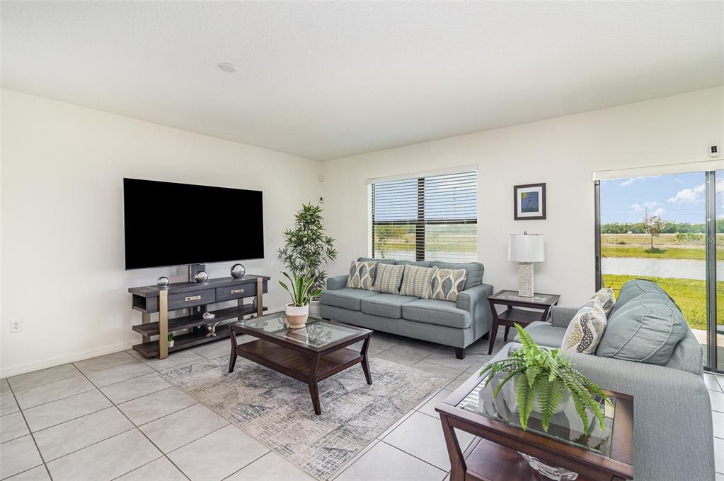 A living room features light tile floors, two blue sofas, a television, and sliding glass doors — 3920 FOGGY MIST ROAD SE, PALM BAY, FL