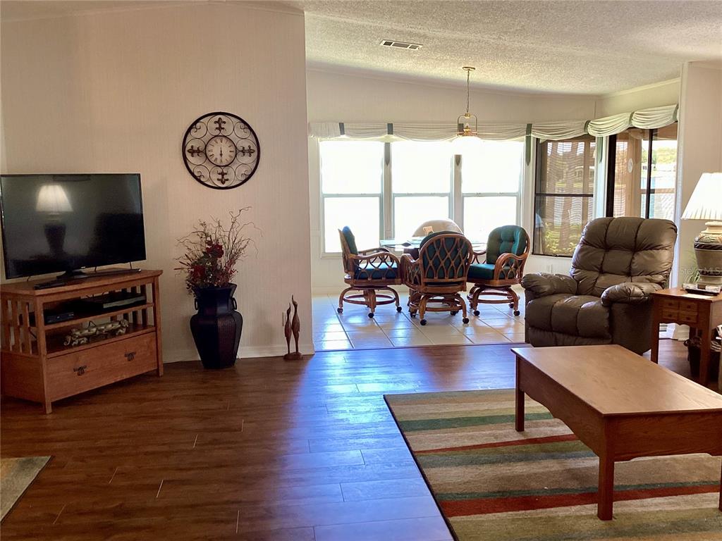 A living room with wood-look flooring, a television console, and a dining area with wicker chairs — 8451 IMPERIAL CIRCLE, PALMETTO, FL